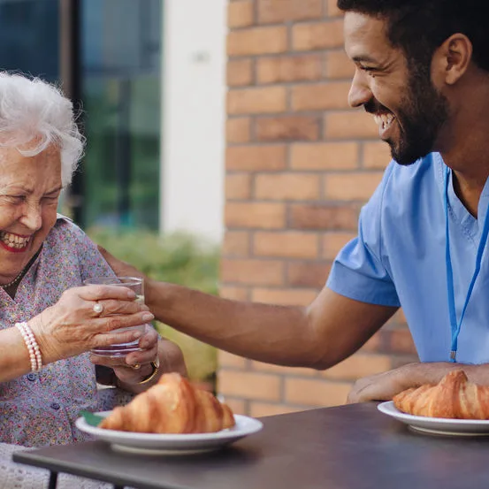 Essen reichen, ausländische Pflegekraft, fröhliche Bewohnerin, Seniorin