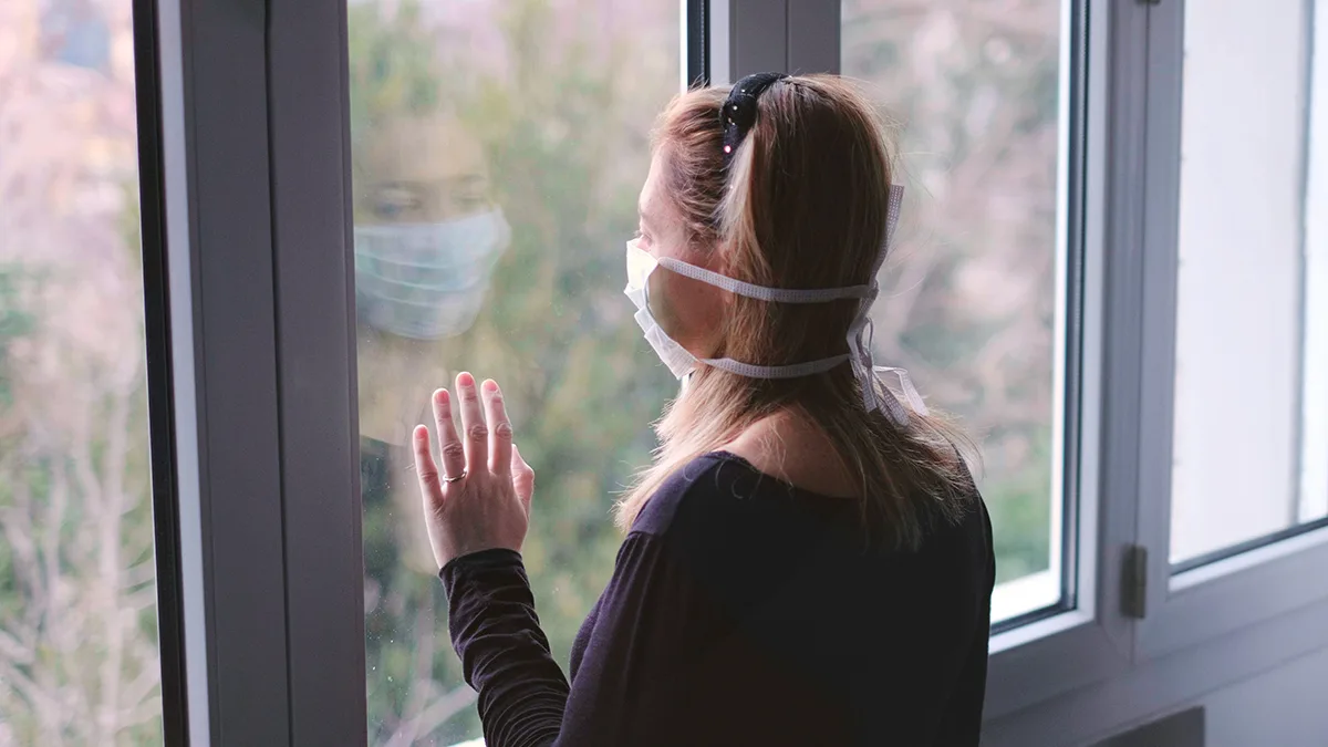 Quarantäne Frau mit Maske am Fenster Foto iStock Luca Lorenzelli Quarantäne Frau mit Maske am Fenster Foto iStock Luca Lorenzelli.jpg